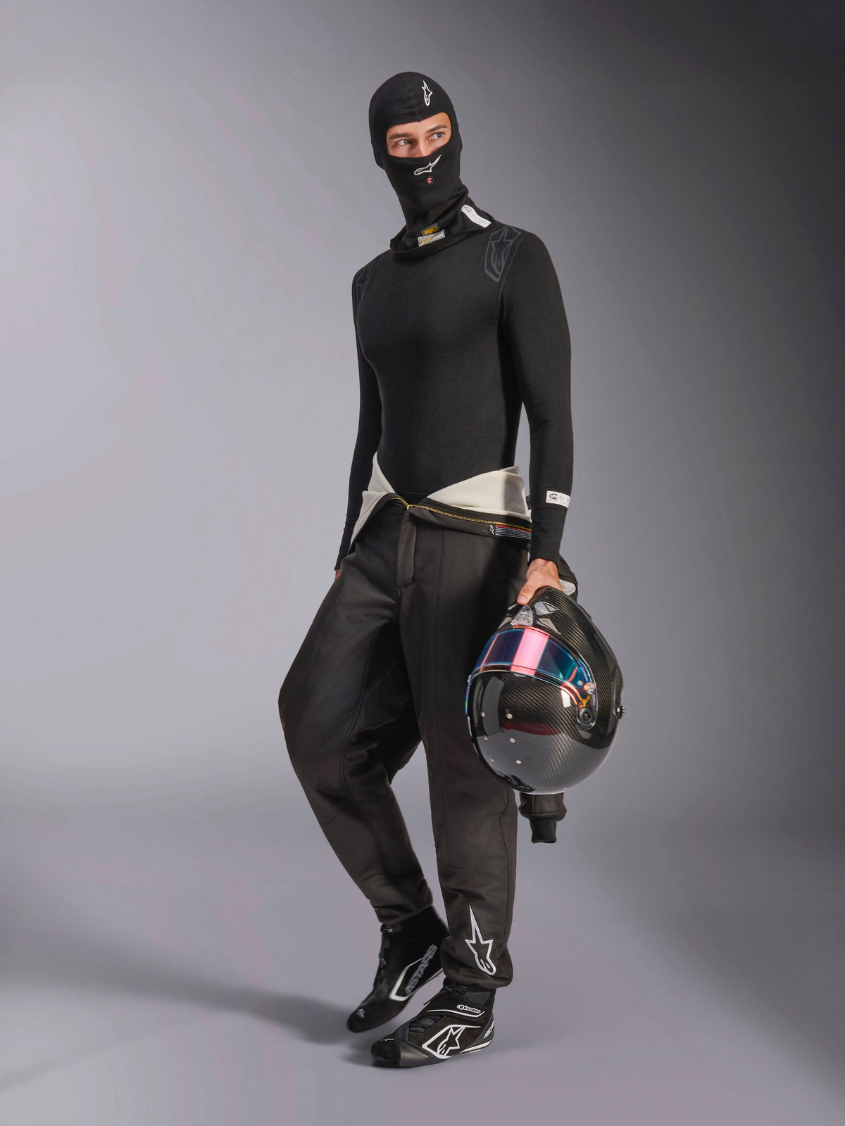 Alpinestars ZX Evo V3 Balaclava, sort, båret af en kører med komplet basislag til motorsport, med det hvide logo i panden, holder en kulfiberhjelm med et iriserende visir, professionel flammebestandig motorsportsbeklædning.