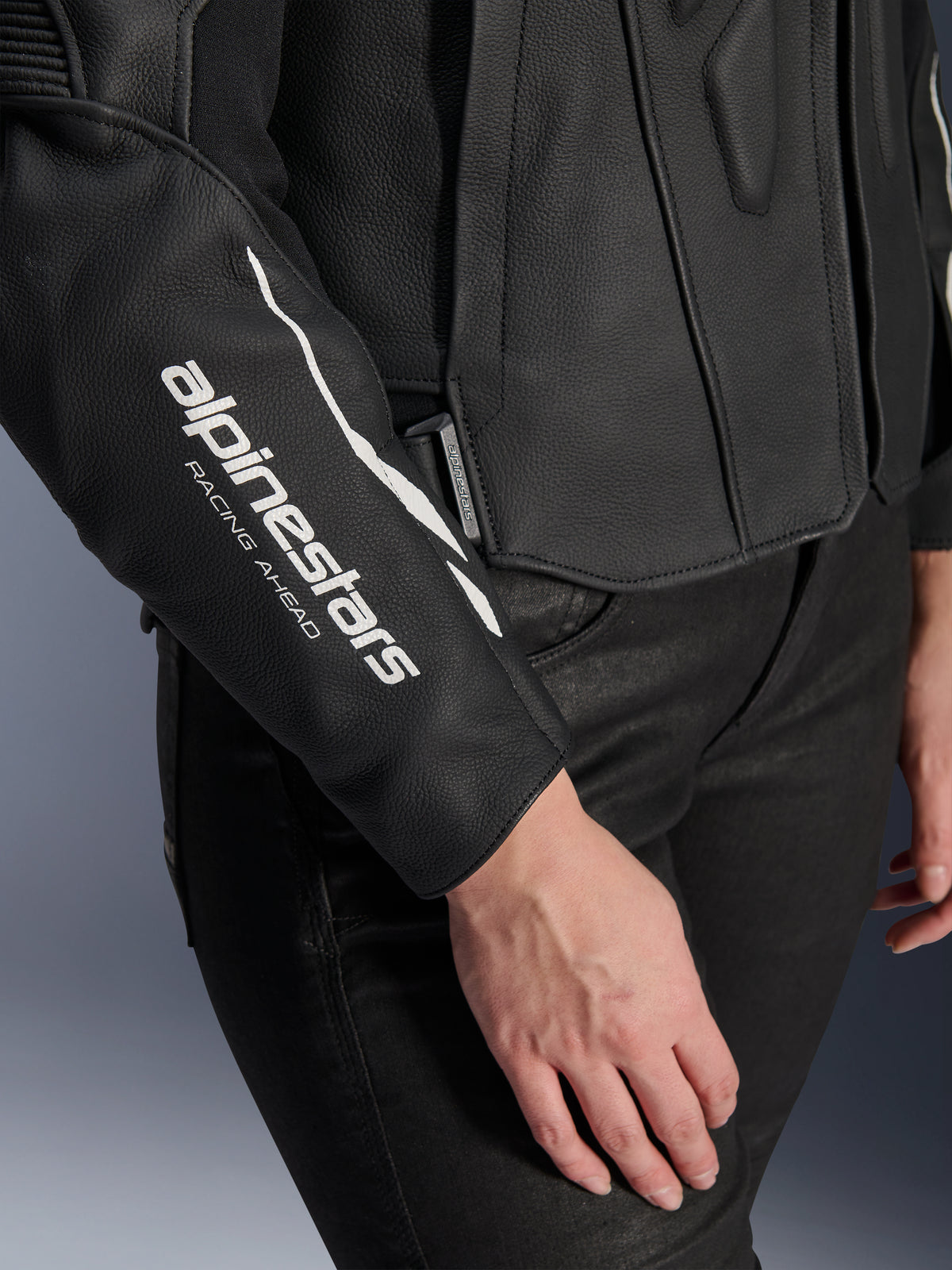 Nærbillede af Alpinestars Stella Dusk læderjakke, sort motorcykellæderjakke til kvinder, med hvidt 'alpinestars RACING AHEAD'-logo på ærmet, førsteklasses bovin lædertekstur, båret med sorte bukser