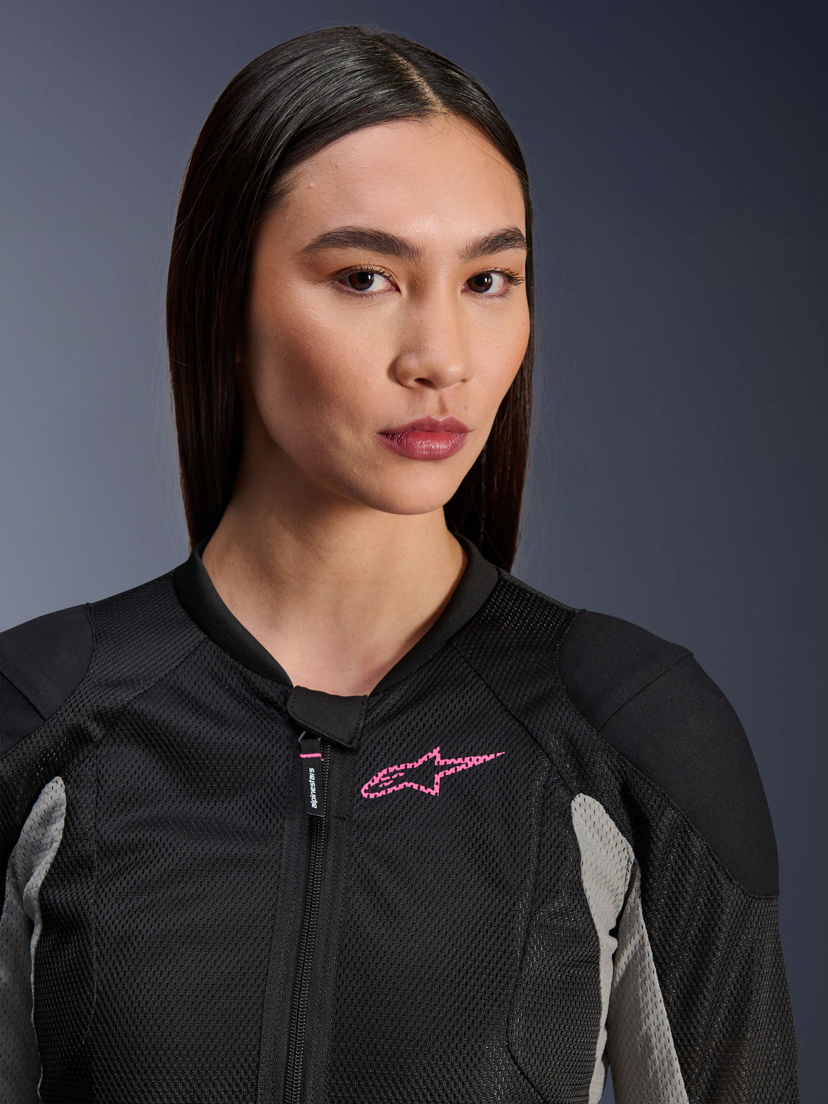 Kvinde iført Alpinestars Stella Troop-Air-jakke, sort, askegrå og pink fluo, nærbillede der fremhæver den tekniske mesh-konstruktion og pink brystlogo, stilfuldt urbant motorcykeludstyr