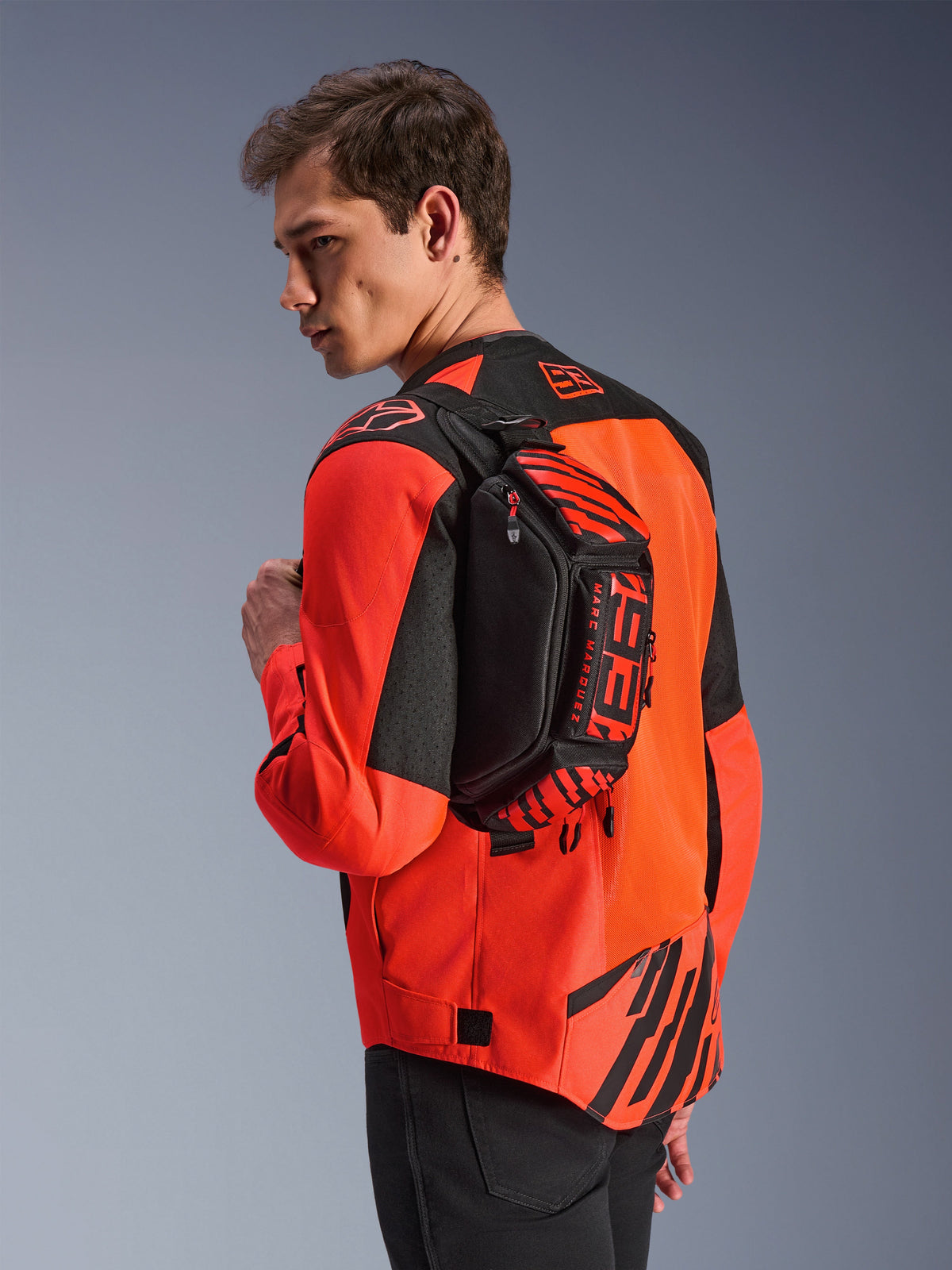 Alpinestars MM93 Waist Bag, Black with Red Fluo and Bright Red, worn by a model across the back over a red and black motorcycle jacket, featuring bold MM93 branding and Marc Marquez graphics