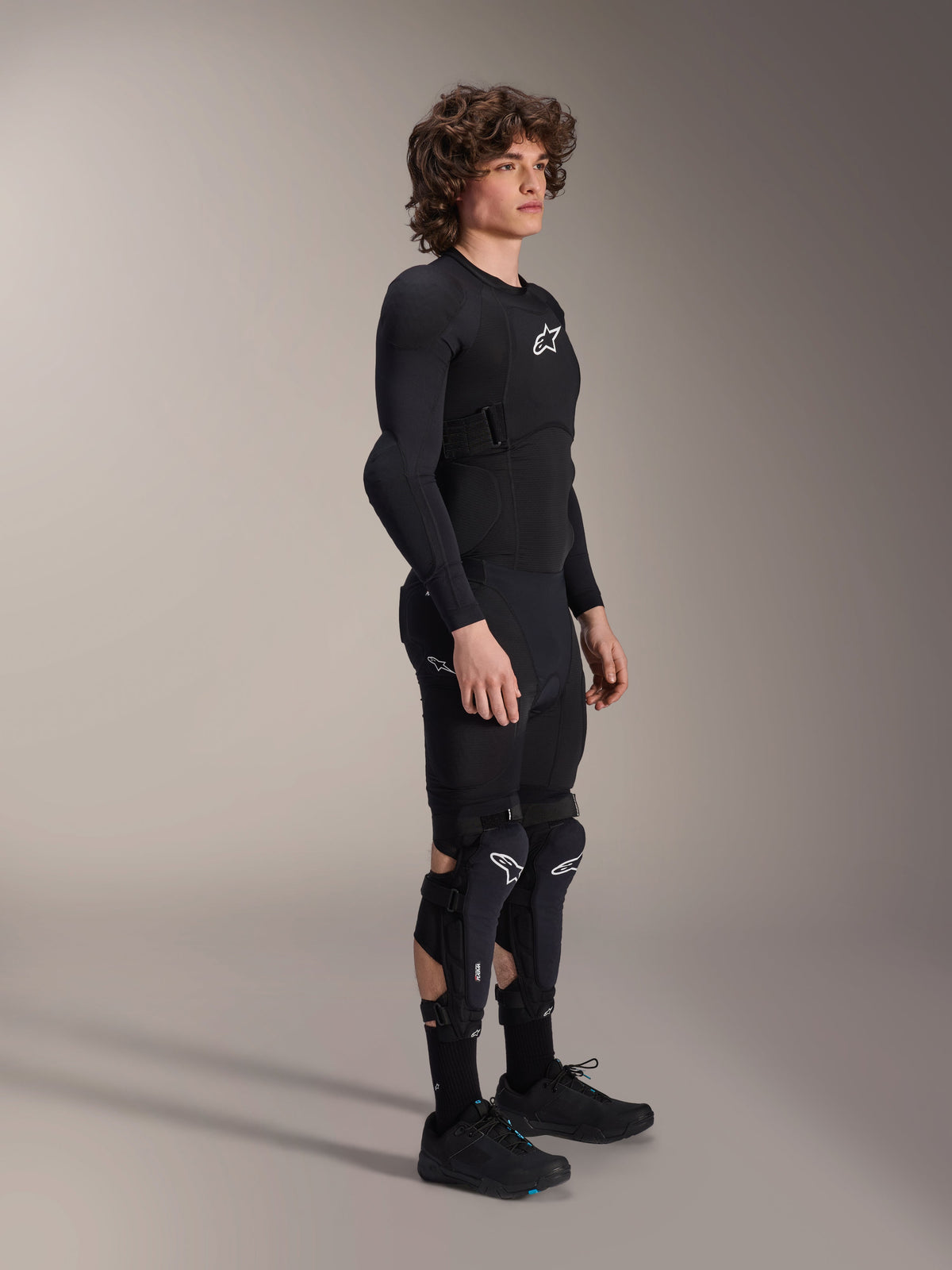 Alpinestars A-Impact Plasma beskyttelsesjakke – langærmet, sort, båret af en model med matchende beskyttelsesudstyr herunder knæbeskyttere og shorts, med hvide Astars-logoer, åndbar mesh-konstruktion og strømlinet design til off-road cykling