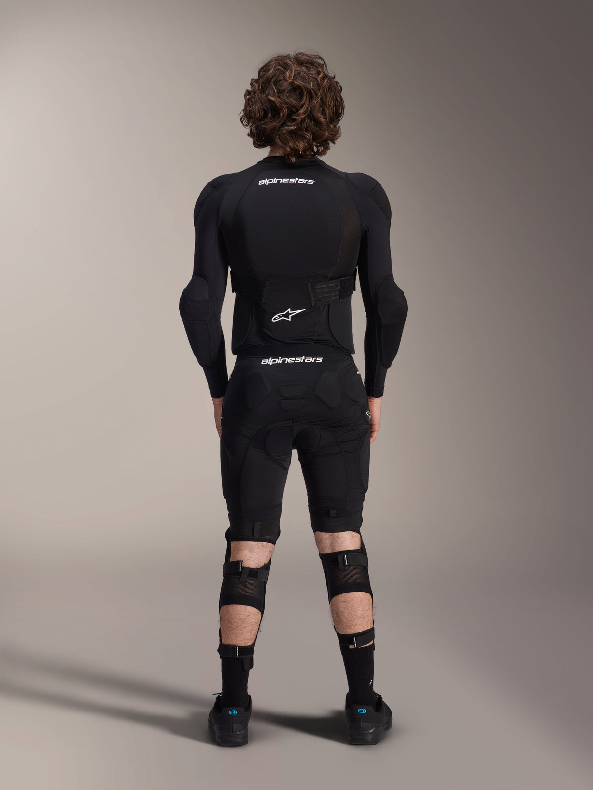 Alpinestars A-Impact Plasma Beskyttelsesjakke - Langærmet, set bagfra, sort med hvide Alpinestars-logoer, båret med beskyttelsesshorts og knæbeskyttere for fuld kropsbeskyttelse til mountainbike