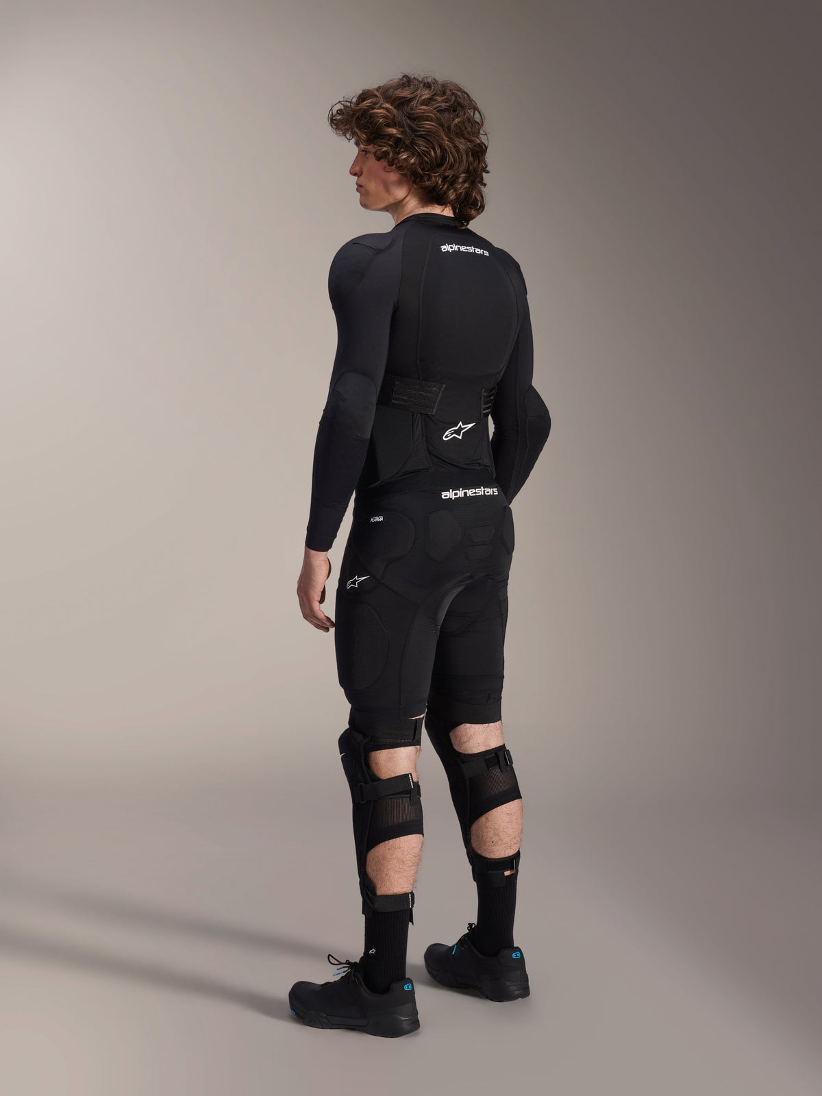Alpinestars A-Impact Plasma Protection Jacket - langærmet, sort med hvide logoer, set bagfra på en model, integreret rygbeskytter, åndbart mesh-chassis, kombineret med mountainbike-beskyttelsesshorts og knæbeskyttere