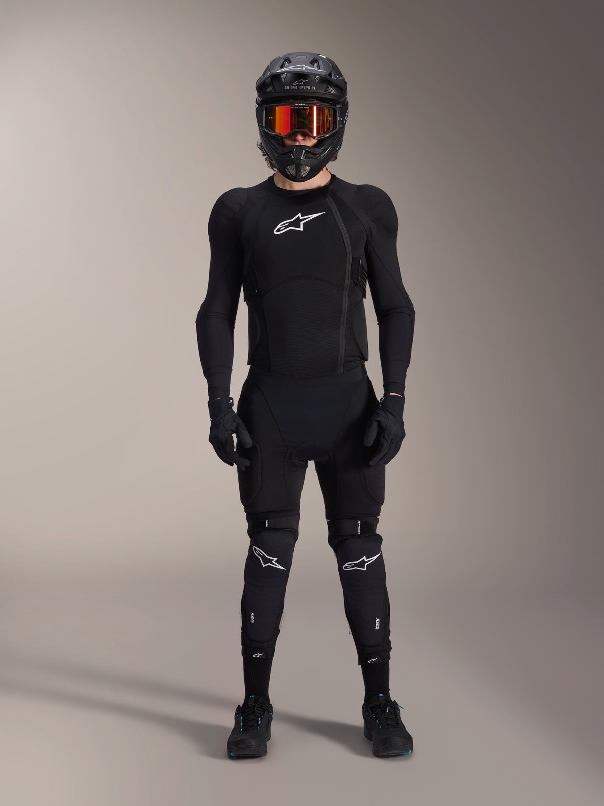 Mountainbike-rytter iført komplet beskyttelsesudstyr, Alpinestars A-Impact Plasma beskyttelsesjakke i sort og hvid, med hvidt brystlogo og mesh-stof, kombineret med sort hjelm, rødtonede goggles og knæbeskyttere, koordineret high-performance MTB-beskyttelsessæt.