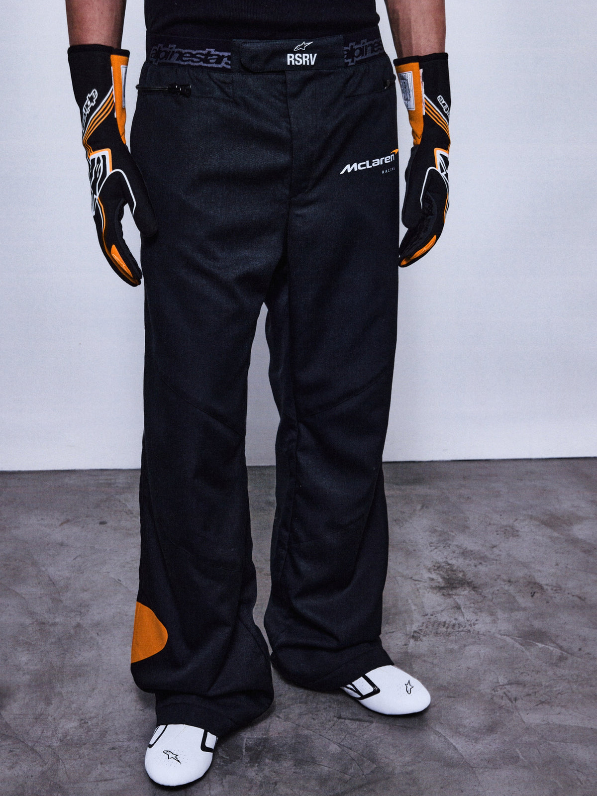 Alpinestars RSRV Arena Suit bukser, racerbukser til motorcykel, sort med orange detaljer, McLaren-logoer, premium beskyttelsesudstyr, vist med matchende handsker og racerstøvler