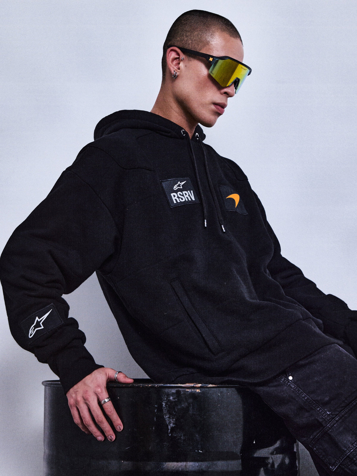 Alpinestars RSRV Rival hættetrøje, sort premium streetwear hoodie med RSRV-logo og patches, unisex design, person iført reflekterende solbriller og smykker, urban lifestyle