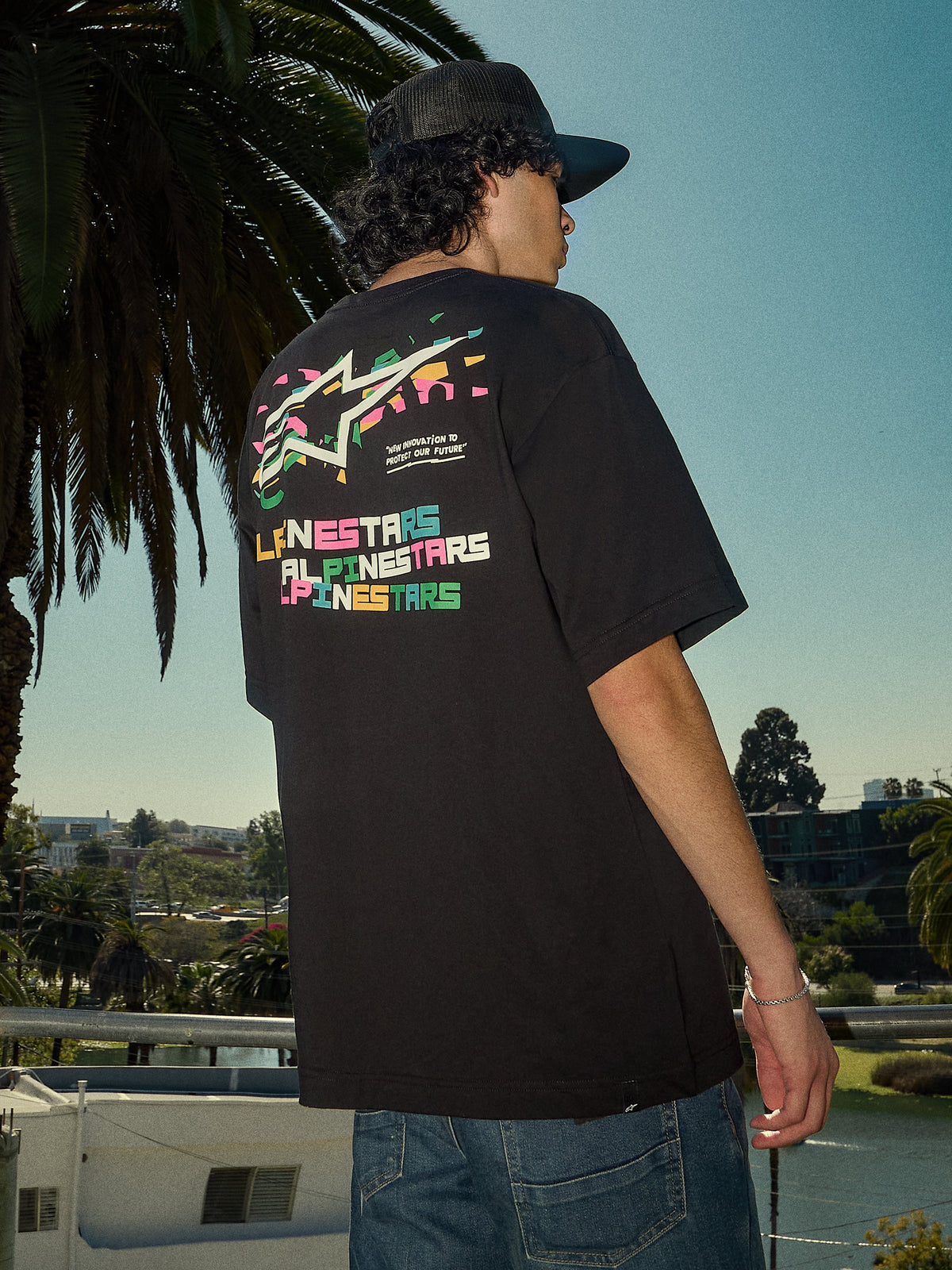 Alpinestars Wild Oversized CSF Tee, kortærmet T-shirt, sort, livligt flerfarvet Astars-logo på ryggen, oversized pasform, afslappet streetwear-livsstilsbillede med palmetræer