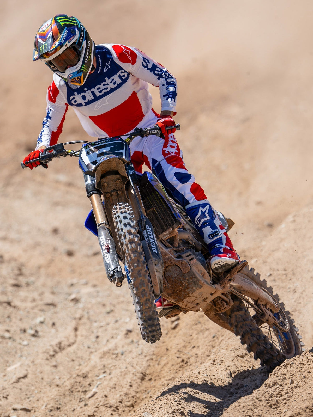 Motocrosskører i aktion på en jordbane, iført Limited Edition Techstar Fortitude-trøje i rød, hvid og blå, matchende racerbukser og støvler, markant Alpinestars-branding, professionelt off-road racertøj