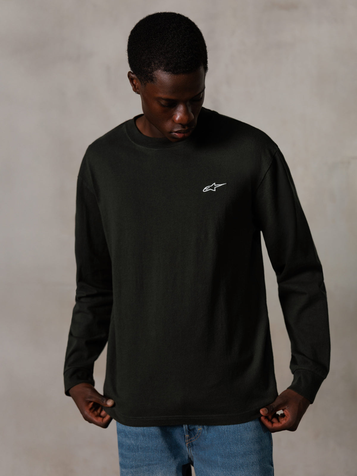 Alpinestars Essentials Ageless LS Tee, langærmet T-shirt, Off Black, med et lille hvidt logo på brystet, båret af en model i blå jeans, casual lifestyle streetwear