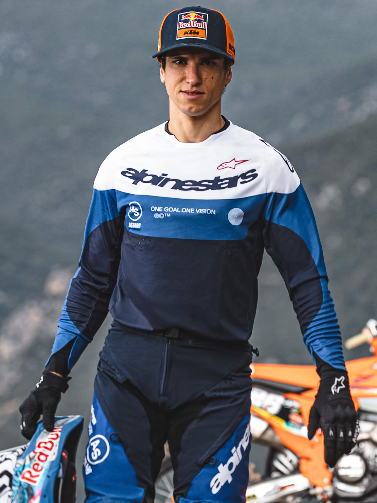 Motocross-rytter iført Alpinestars Pro-Dura Jersey i navy, klar blå og hvid, med Alpinestars-navnetræk og 'One Goal. One Vision.' slogan, kombineret med matchende køreudstyr og en Red Bull KTM-kasket i udendørs omgivelser.