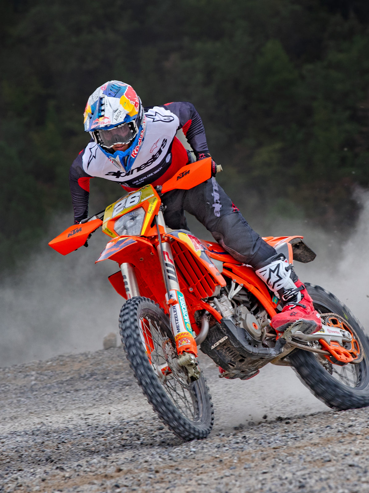 Motocross-rytter i aktion iført Alpinestars Pro-Dura Jersey i sort, rød og hvid, kører på en orange motocross-cykel på en støvet off-road-sti, kombineret med sorte bukser og rød-hvide støvler