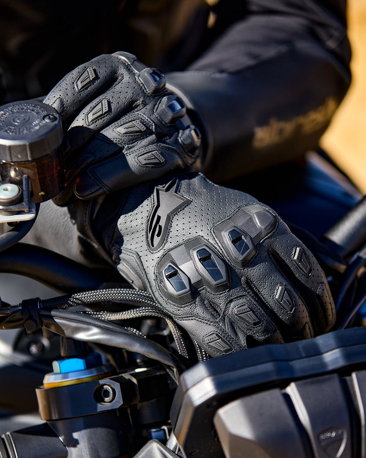 Alpinestars SP X 7 sorte motorcykelhandsker i perforeret læder med TPU-knobeskyttelse på et motorcykelstyr.