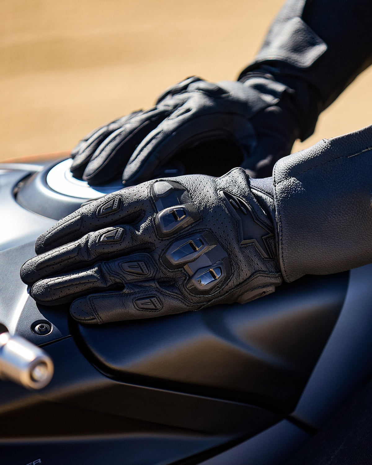Alpinestars SP X 7 handsker, sorte motorcykelhandsker i perforeret læder med TPU-knoer, hvilende på en benzintank.