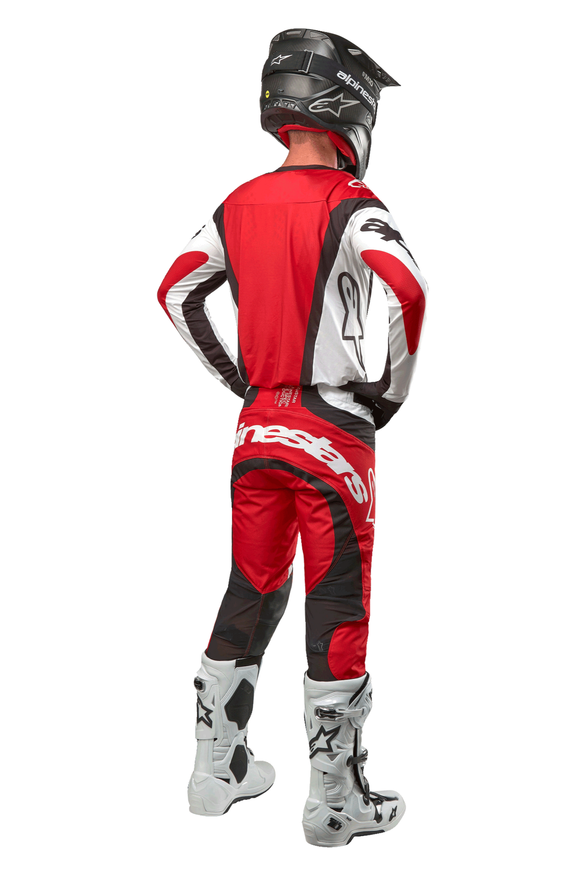 Alpinestars 2024 Techstar Ocuri bukser, motocrossbukser, Mars rød, hvid og sort, set bagfra af en motocrosskører iført fuldt racerudstyr, herunder matchende trøje, sort hjelm og hvide og sorte støvler, hvilket fremhæver Alpinestars-branding og den slidstærke tekstilkonstruktion.