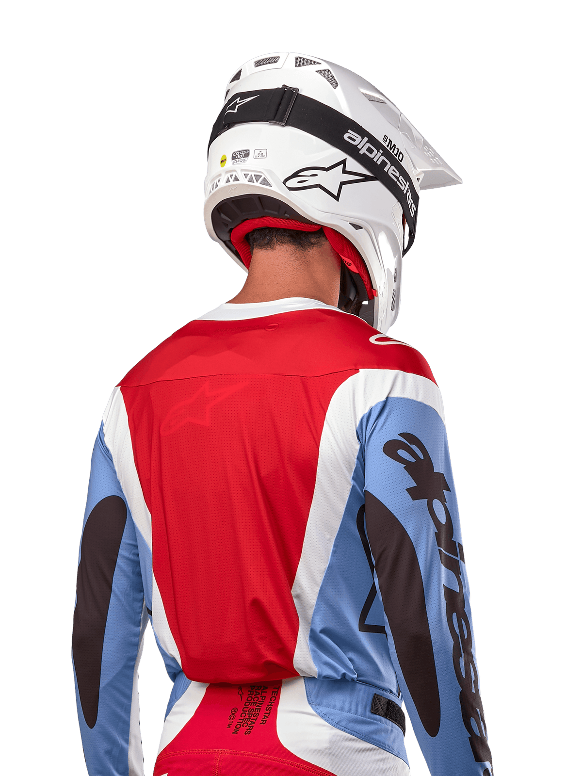 Alpinestars 2024 Techstar Ocuri trøje, motocross-trøje, lyseblå, mars-rød og hvid, set bagfra af kører med matchende hvid hjelm og sorte briller, har markant sort branding på ærmerne og ergonomisk race-pasform til off-road-præstationer