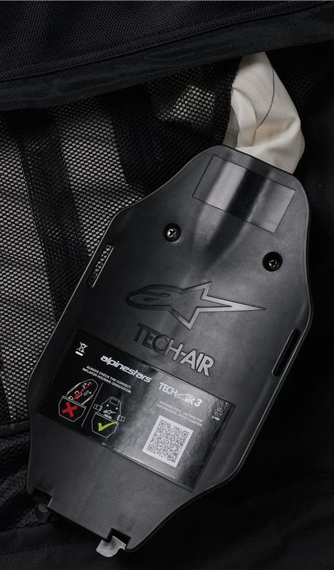 Alpinestars Tech-Air 3 V2 System, indvendig visning af gasinflator- og ECU-huset, sort plast med præget logo, sikkerhedsmærkat med QR-kode og installationsdiagrammer, sort mesh-inderfor, detalje af det brugerservicerbare autonome airbagsystem
