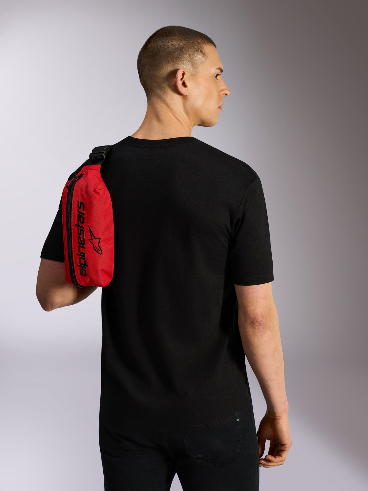 Alpinestars Only Linear hoftebæltetaske, rød og sort, båret over skulderen som en sling-bag af en model i en sort t-shirt, med lodret lynlås og sort Alpinestars-branding, holdbart urbant tilbehør.