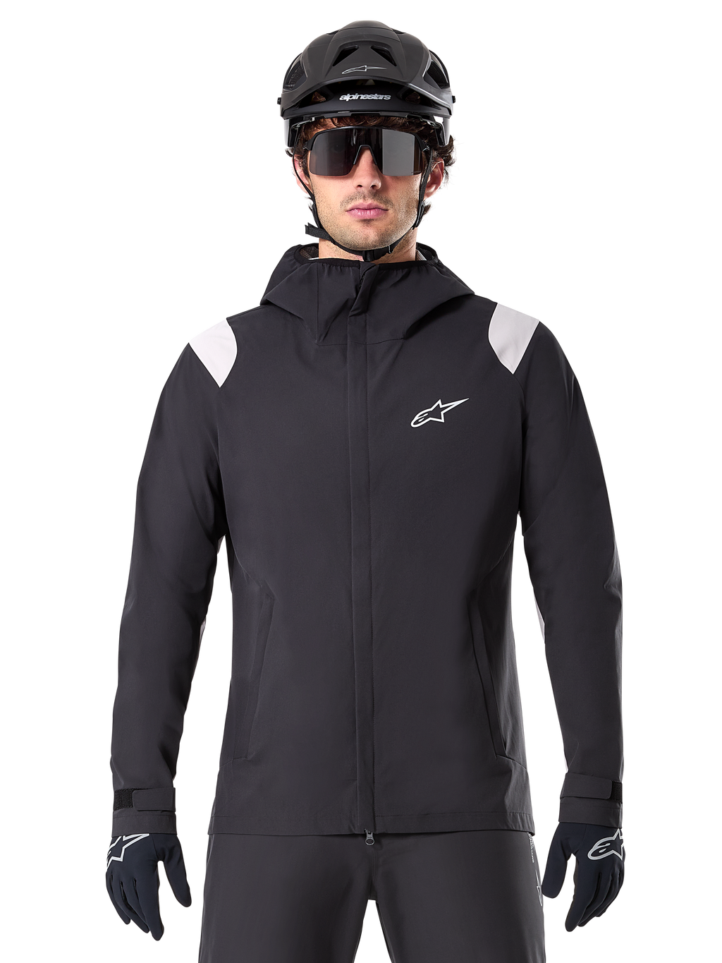 Alpinestars A-Dura regnjakke, MTB-regnjakke, sort med hvide skulderpaneler, bæres med sort MTB-hjelm, solbriller og handsker, vandtæt design med hætte og lynlås foran, sporty udendørsudstyr til cykling