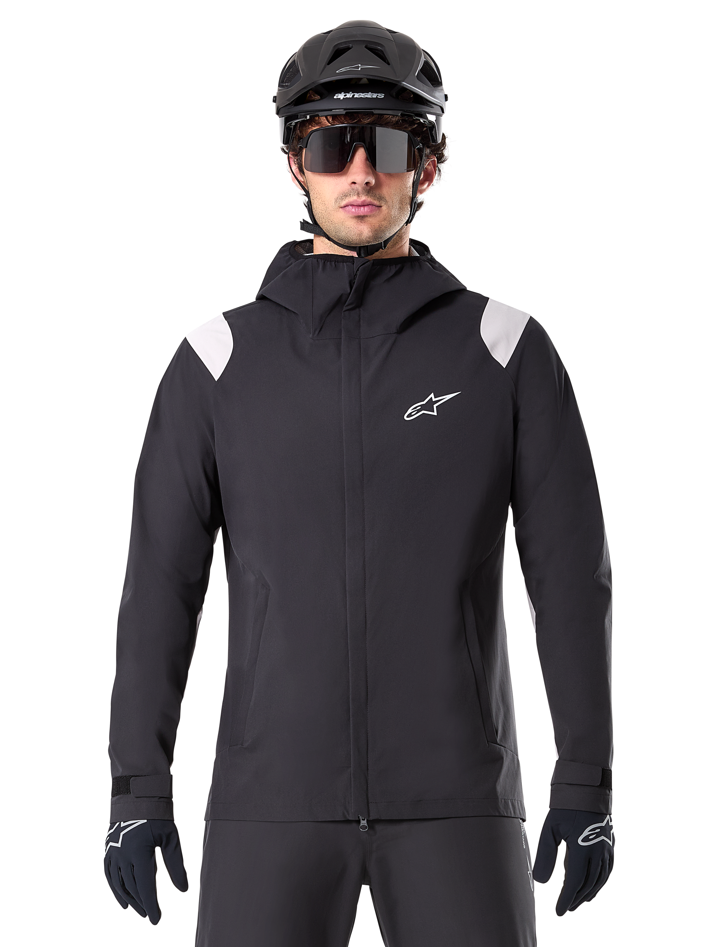 Alpinestars A-Dura regnjakke, MTB-regnjakke, sort med hvide skulderpaneler, bæres med sort MTB-hjelm, solbriller og handsker, vandtæt design med hætte og lynlås foran, sporty udendørsudstyr til cykling