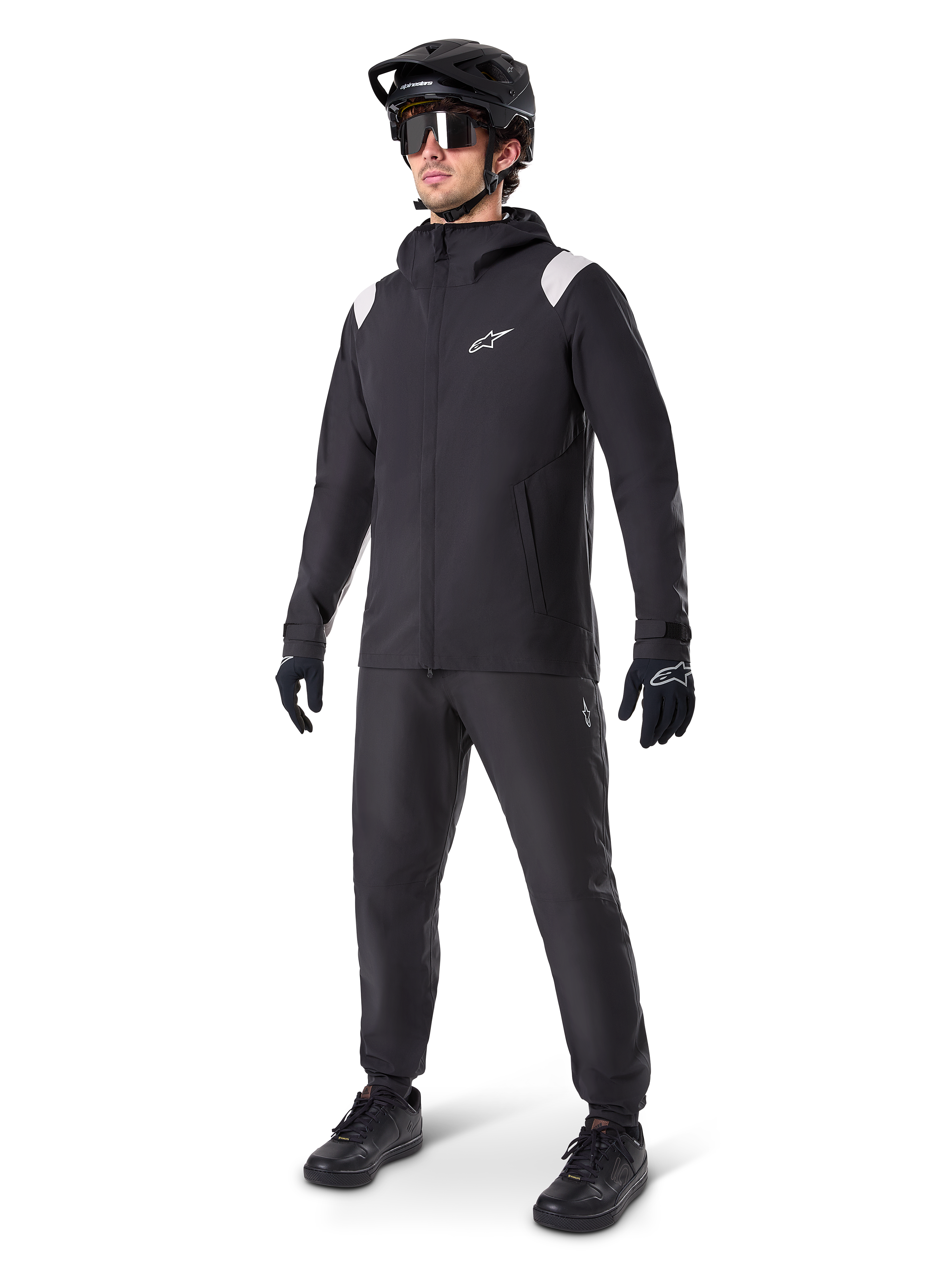 Alpinestars A-Dura regnjakke, sort mountainbike-regnjakke, med hvide skulderdetaljer, båret af en rytter med matchende sort MTB-hjelm, solbriller, handsker og bukser, teknisk cykeloutfit til alt slags vejr