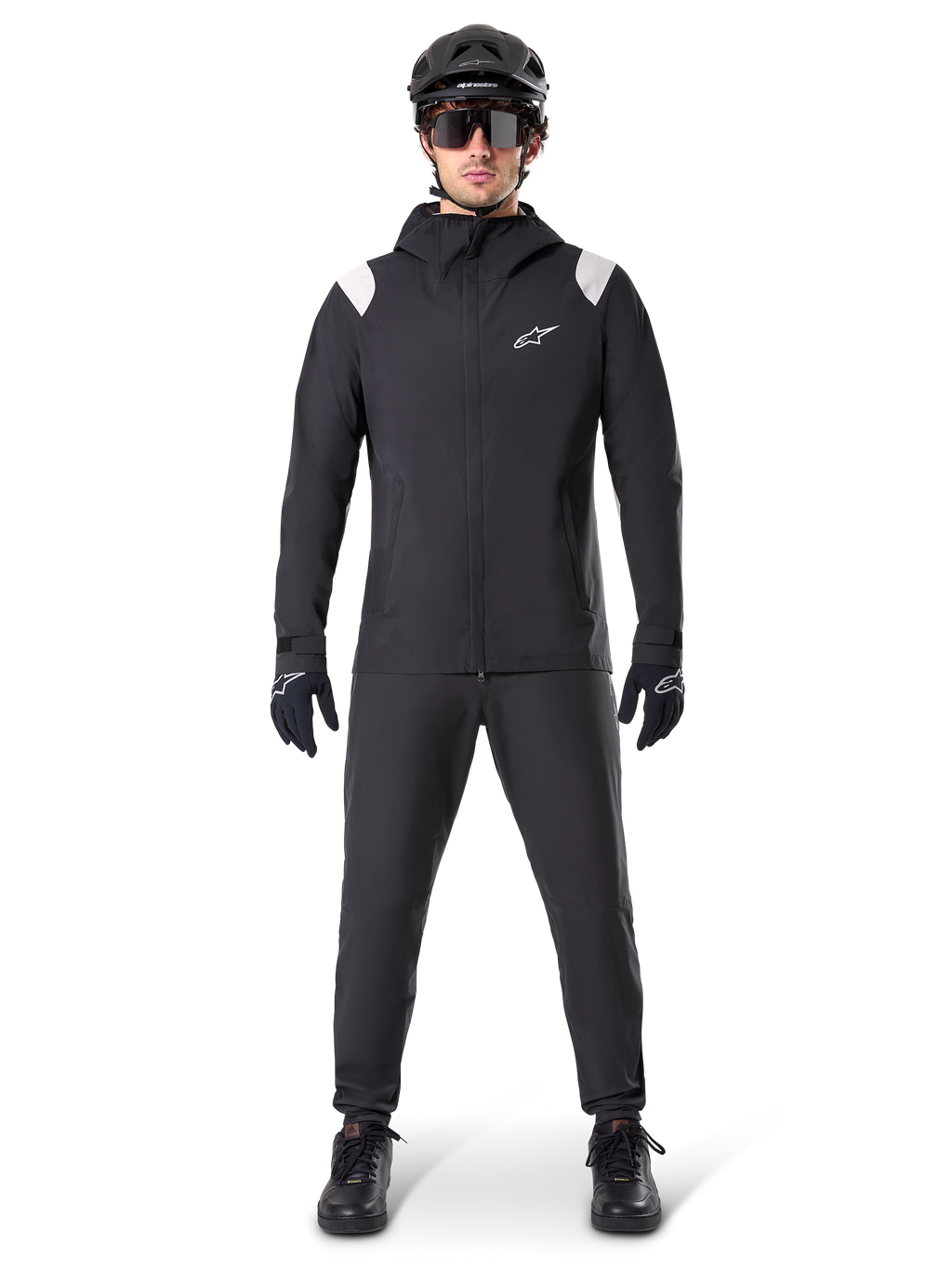 Alpinestars A-Dura regnjakke, mountainbike-regnjakke, sort med hvide skulderdetaljer og hvidt logo på brystet, bæres med sorte bukser, sort hjelm, solbriller og handsker, koordineret mountainbike-udstyr til vådt vejr