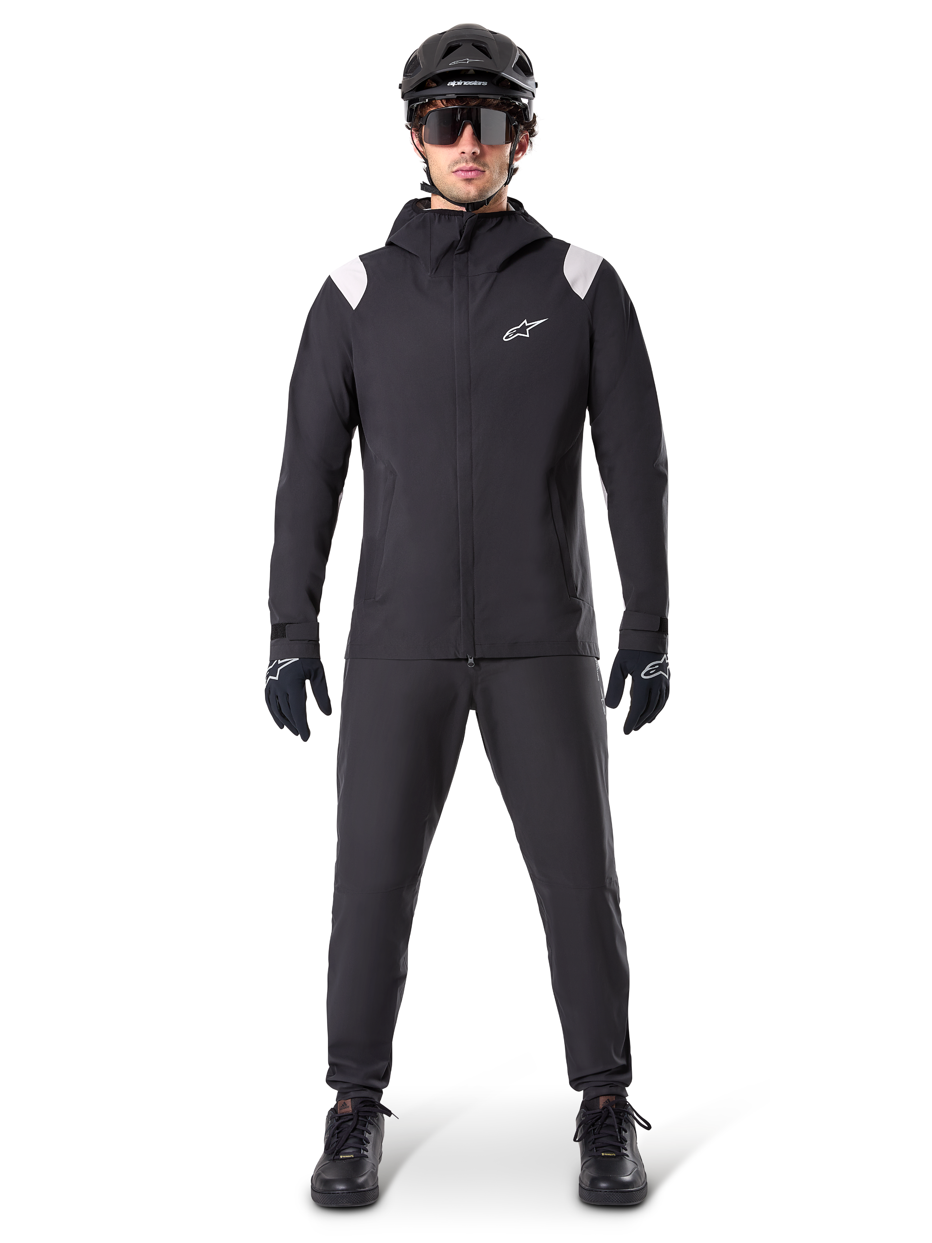 Alpinestars A-Dura regnjakke, mountainbike-regnjakke, sort med hvide skulderdetaljer og hvidt logo på brystet, bæres med sorte bukser, sort hjelm, solbriller og handsker, koordineret mountainbike-udstyr til vådt vejr