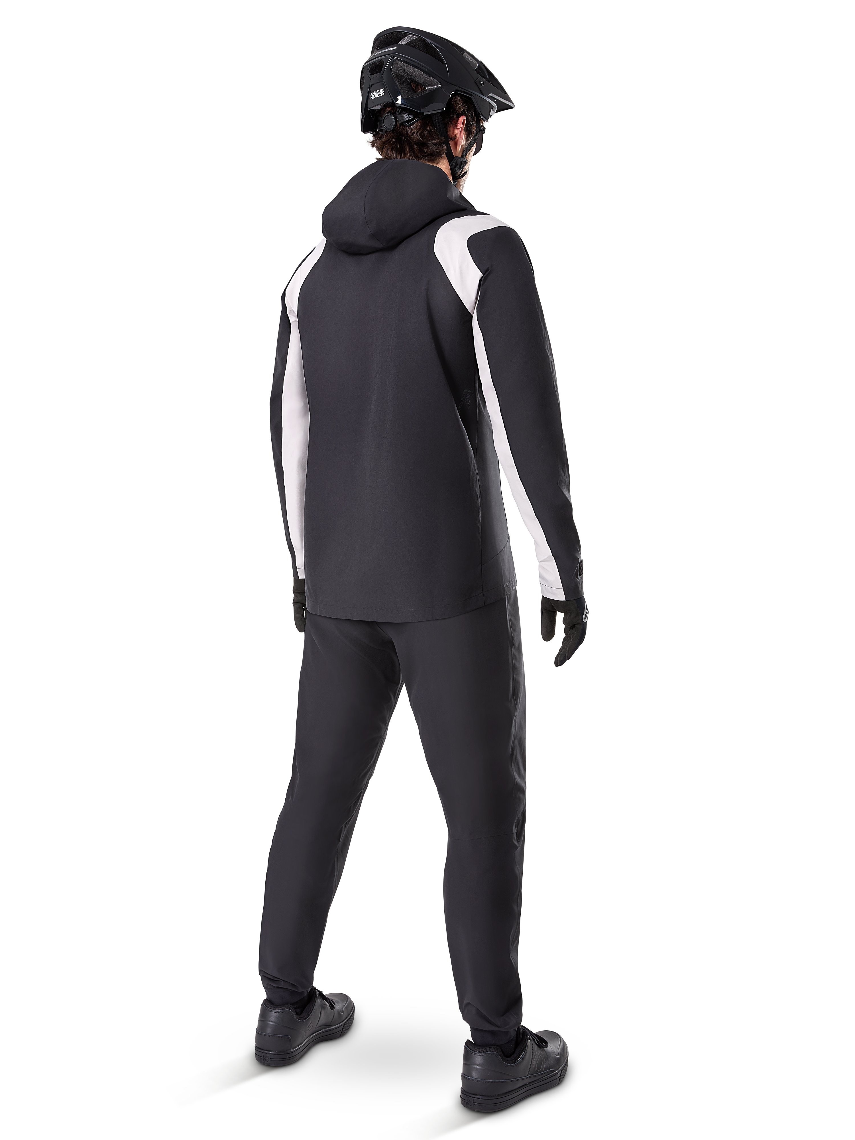 Alpinestars A-Dura Rain Jacket, set bagfra af en mandlig cyklist iført den sort-hvide vandtætte MTB-jakke, matchende sorte cykelbukser, sort hjelm og handsker, teknisk udstyr til mountainbike under våde forhold