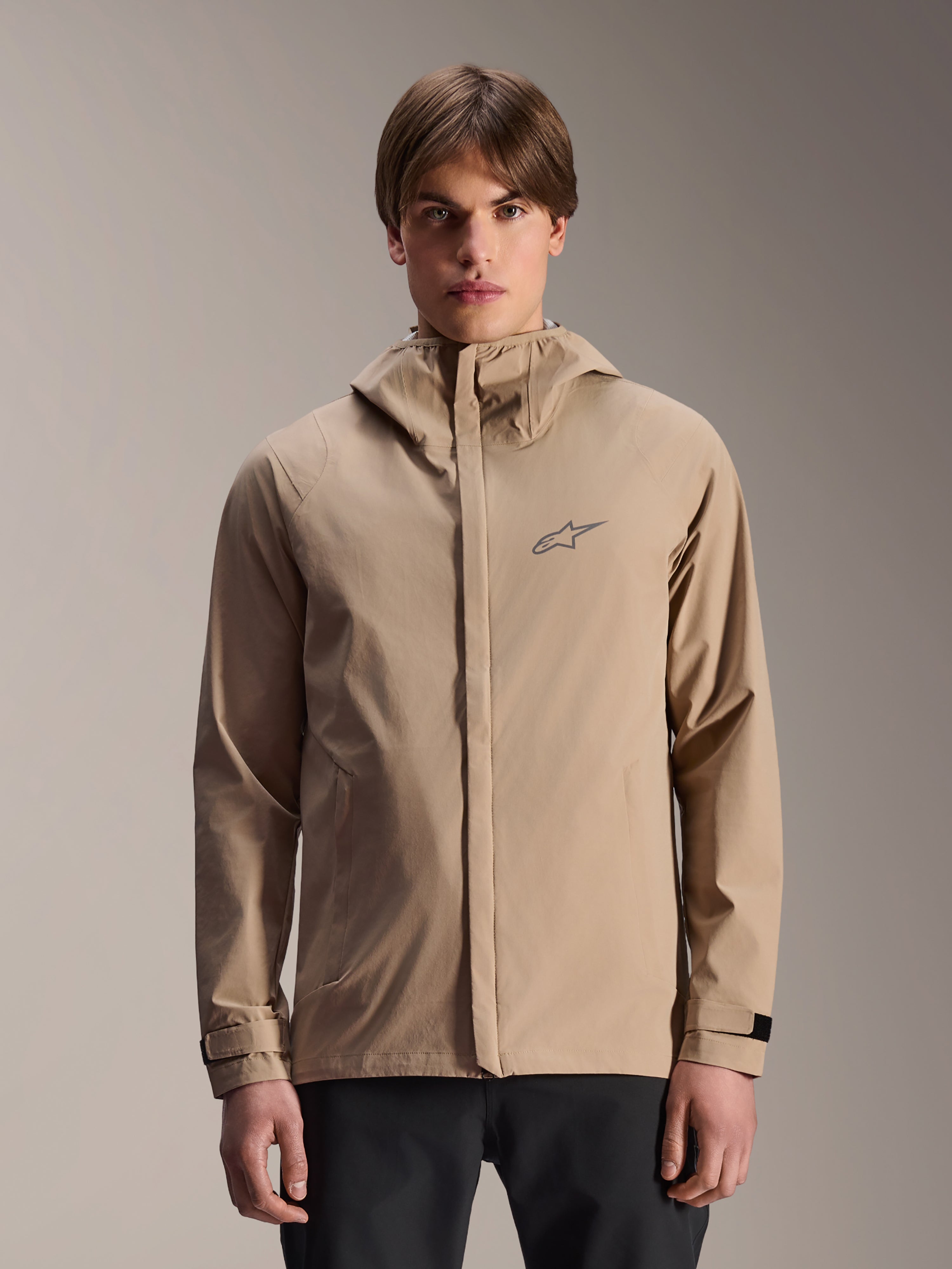 Alpinestars A-Dura Rain Jacket, lysebrun mountainbike-regnjakke med hætte, båret af en model, med lille logo på brystet, justerbare manchetter og skjult lynlås foran, vandtæt cykeludstyr