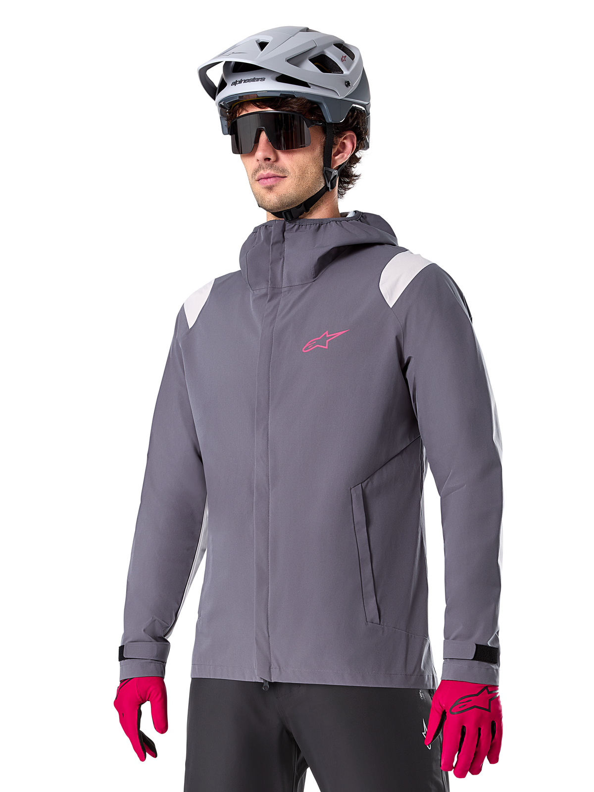Alpinestars A-Dura Rain Jacket, Mountain Bike Rain Jacket, Dark Titanium Gray with pink logo and white shoulder accents, hooded design with front pockets, worn with pink gloves and a light gray cycling helmet