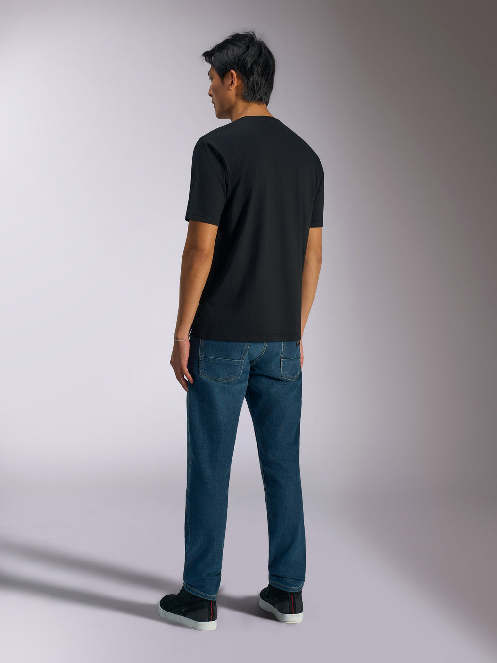 Alpinestars Ageless Shadow CSF Tee, kortærmet t-shirt, sort, set bagfra, båret med blå jeans og sorte sneakers, afslappet motorsport-inspireret streetwear
