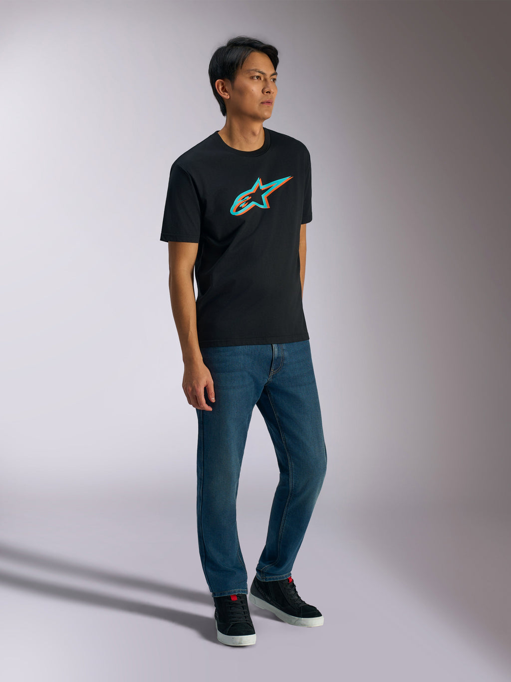 Alpinestars Ageless Shadow CSF Tee, kortærmet T-shirt, sort med turkis og orange shadow-logo, båret af mandlig model med blå jeans og sorte sneakers, afslappet motorsport-inspireret streetwear