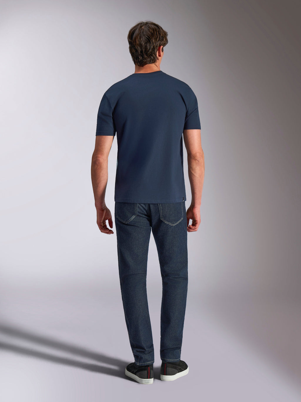 Alpinestars Ageless Shadow CSF Tee, kortærmet t-shirt, navyblå, set bagfra på en model med mørke jeans og sorte sneakers, afslappet motorsport-streetwear.
