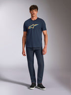 Alpinestars Ageless Shadow CSF Tee, kortærmet t-shirt, marineblå, med orange og lyseblåt Ageless Shadow-logo, vist på en model med mørke denimjeans og sorte sneakers, afslappet motorsport-inspireret streetwear