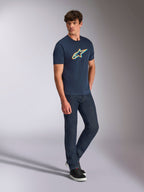 Alpinestars Ageless Shadow CSF Tee, kortærmet t-shirt, navyblå med orange og teal skyggelogo, båret af en model med mørke denimjeans og sorte sneakers, afslappet motorsport-streetwear