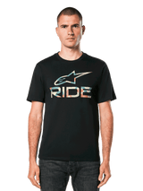 A person stands facing forward, wearing the Alpinestars Ride 4.0 Camo CSF Tee. The black T-shirt features a soft hand print with a colorful graphic logo and the word "RIDE" beneath. The person has short hair and a neutral expression. The background is plain black.