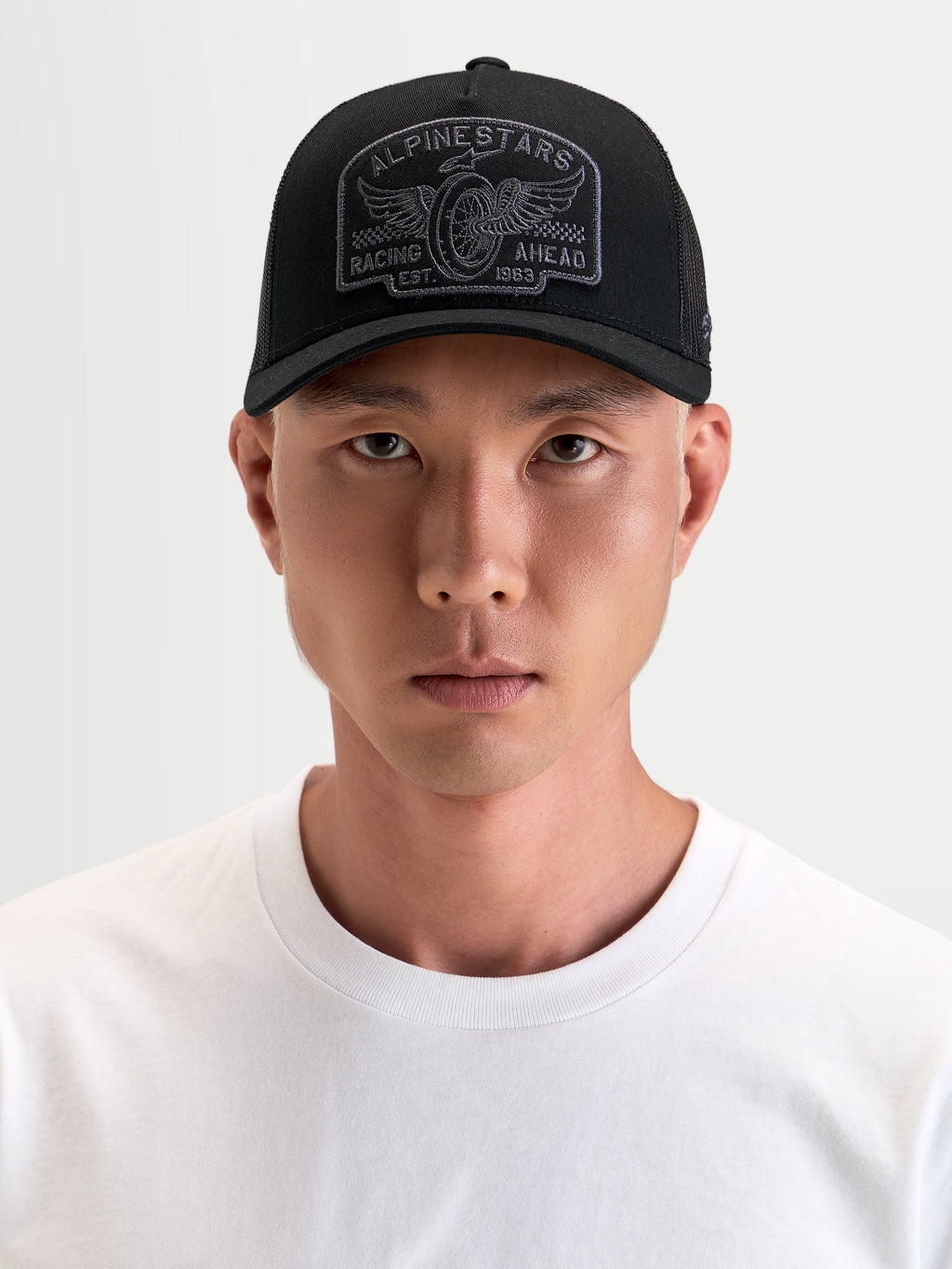 Alpinestars Heritage Patch Trucker Cap, sort og grå trucker cap med buet skygge og broderet logopatch, båret af mandlig model
