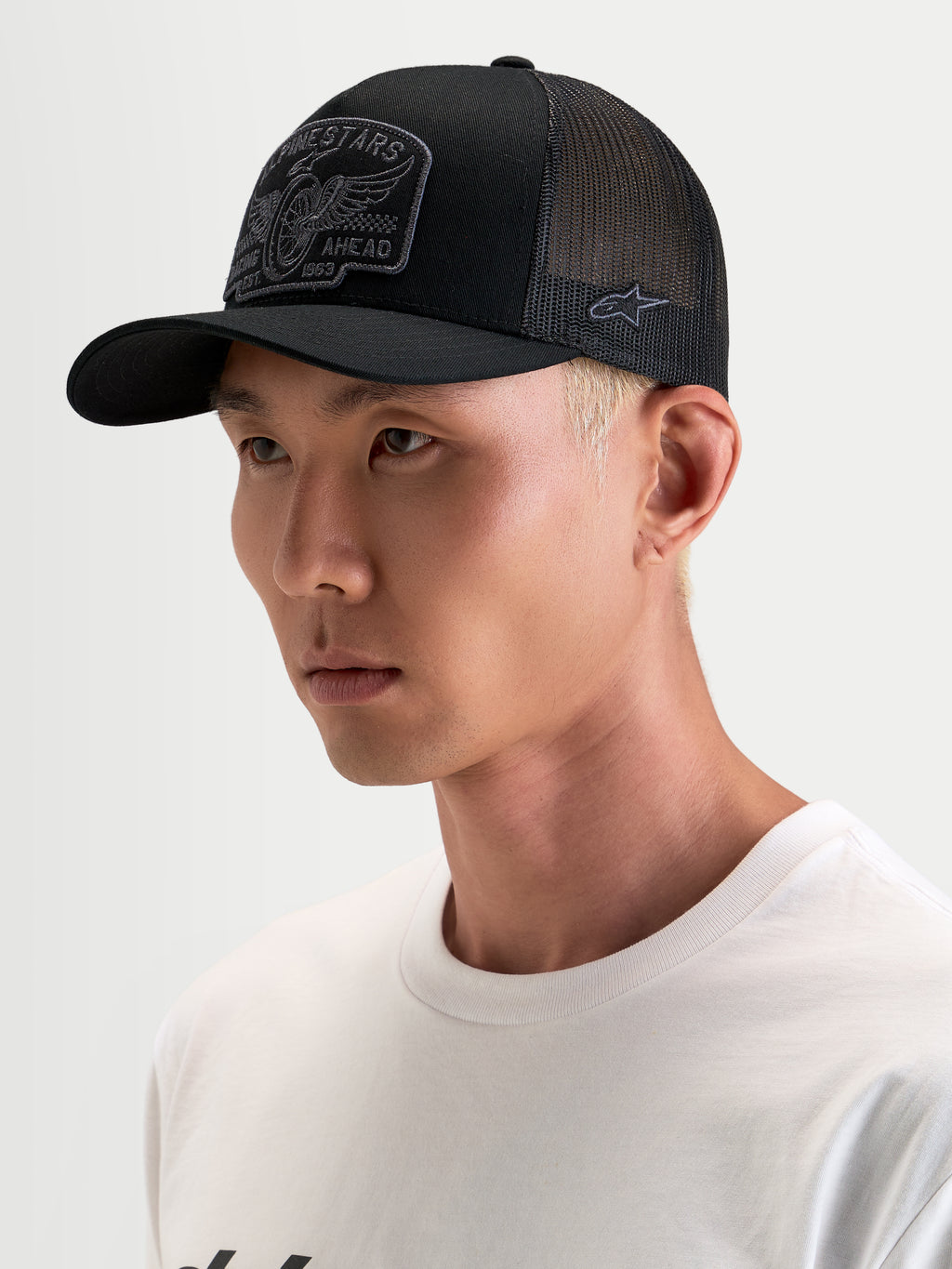 Alpinestars Heritage Patch Trucker Cap, sort og grå kasket til hverdagsbrug, med buet skygge og broderet frontpatch, båret af model