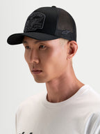 Alpinestars Heritage Patch Trucker Cap, sort og grå kasket til hverdagsbrug, med buet skygge og broderet frontpatch, båret af model