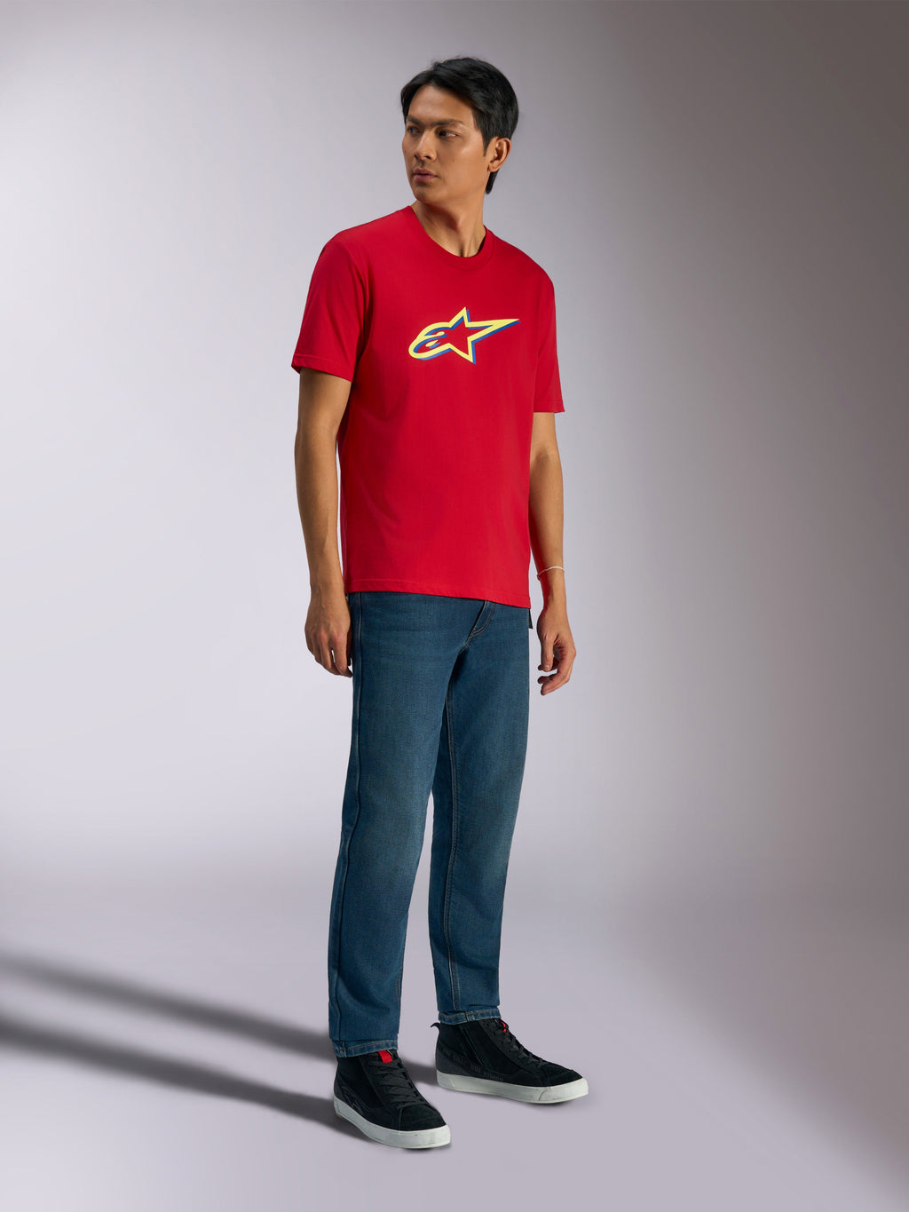Alpinestars Ageless Shadow CSF Tee, kortærmet t-shirt, rød, med Ageless shadow-logo med gule og blå detaljer, vist på model med denimjeans og sorte sneakers, casual motorsport streetwear