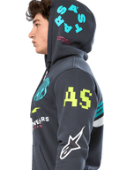 Alpinestars Variegate hættetrøje, gunmetal-grå fleece med lynlås foran, sideprofil af model, multi-logo grafik i neongul, lyseblå og hvid, med 'AS'-branding på ærmet og 'STARS' på hætten, afslappet motorsport-inspireret streetwear
