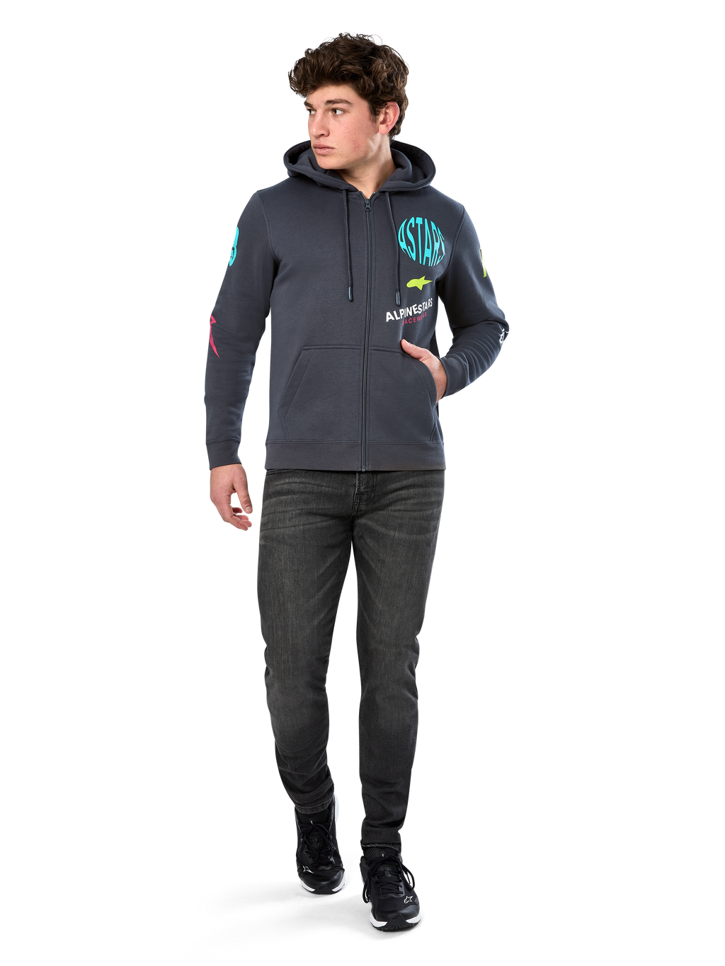 Alpinestars Variegate Hoodie, fleecehættetrøje med lynlås foran, Gunmetal grå, båret af model med sorte jeans og sneakers, med turkis 'ASTARS' branding og farverig logokunst på ærmer og bryst, afslappet motorsport-inspireret streetwear