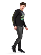 Mand iført Alpinestars Ayess CSF langærmet T-shirt, sort, med gul skrift på ærmet og levende limegrøn og cyan grafik på brystet, kombineret med mørkegrå jeans og sorte sneakers, afslappet motorsport-inspireret streetwear.