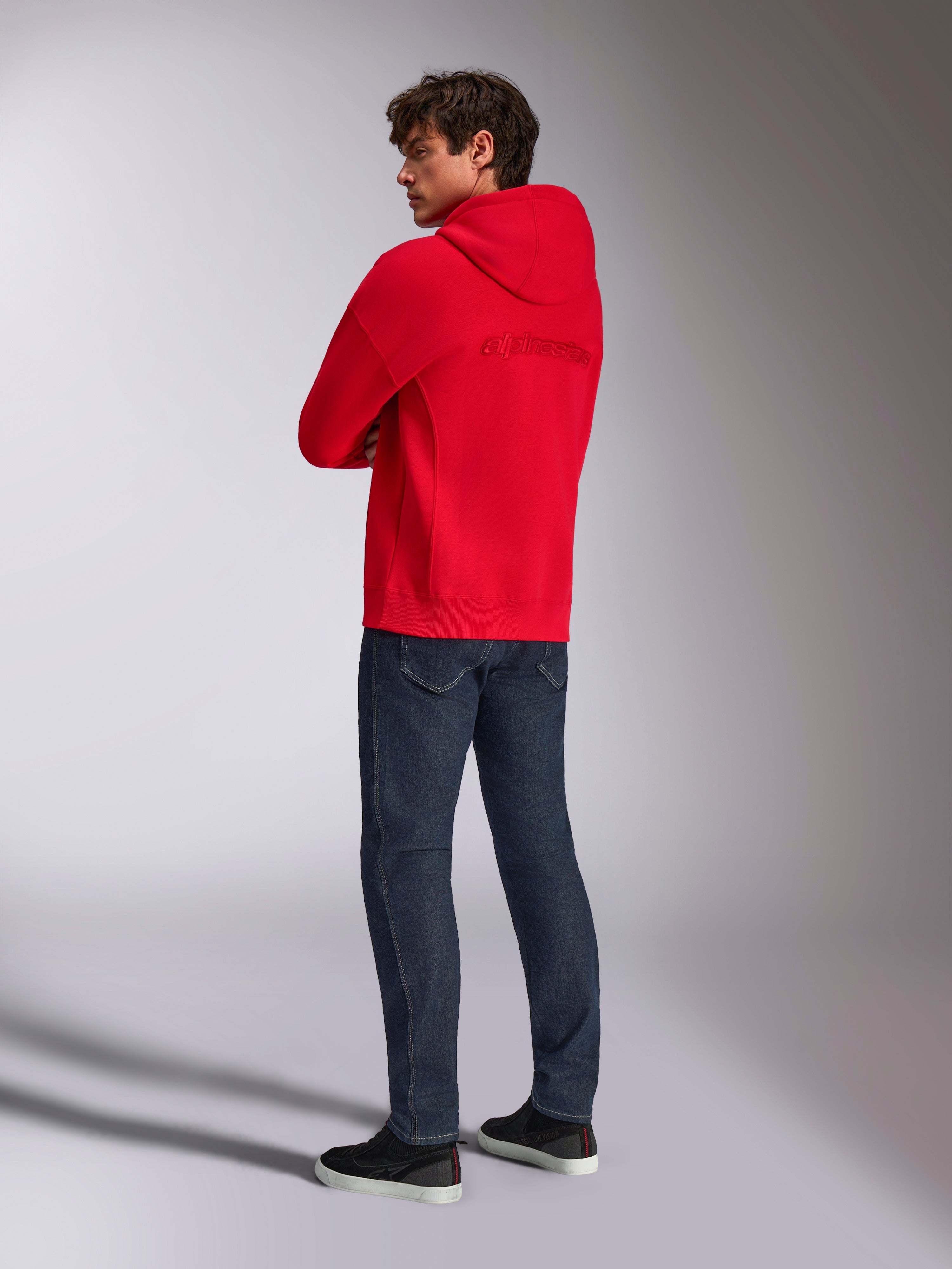 Alpinestars Emergent Oversized hættetrøje, rød, set bagfra med broderet Alpinestars-ordlogo på ryggen, oversized pasform, båret med mørkeblå jeans og sorte sneakers, afslappet lifestyle streetwear