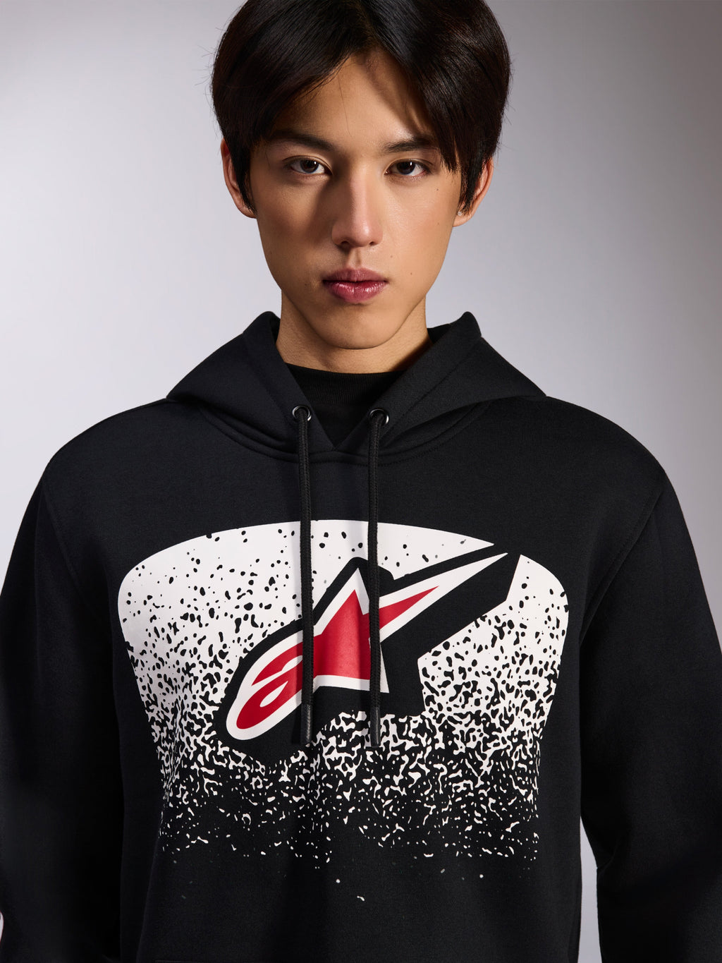 Alpinestars Obsessed hættetrøje, sort pullover i fleece, med et rødt og hvidt Astars-logo inde i en hvid prikket MX-graduering på brystet, båret af en model, afslappet motorsport-streetwear med justerbar hætte med snoretræk
