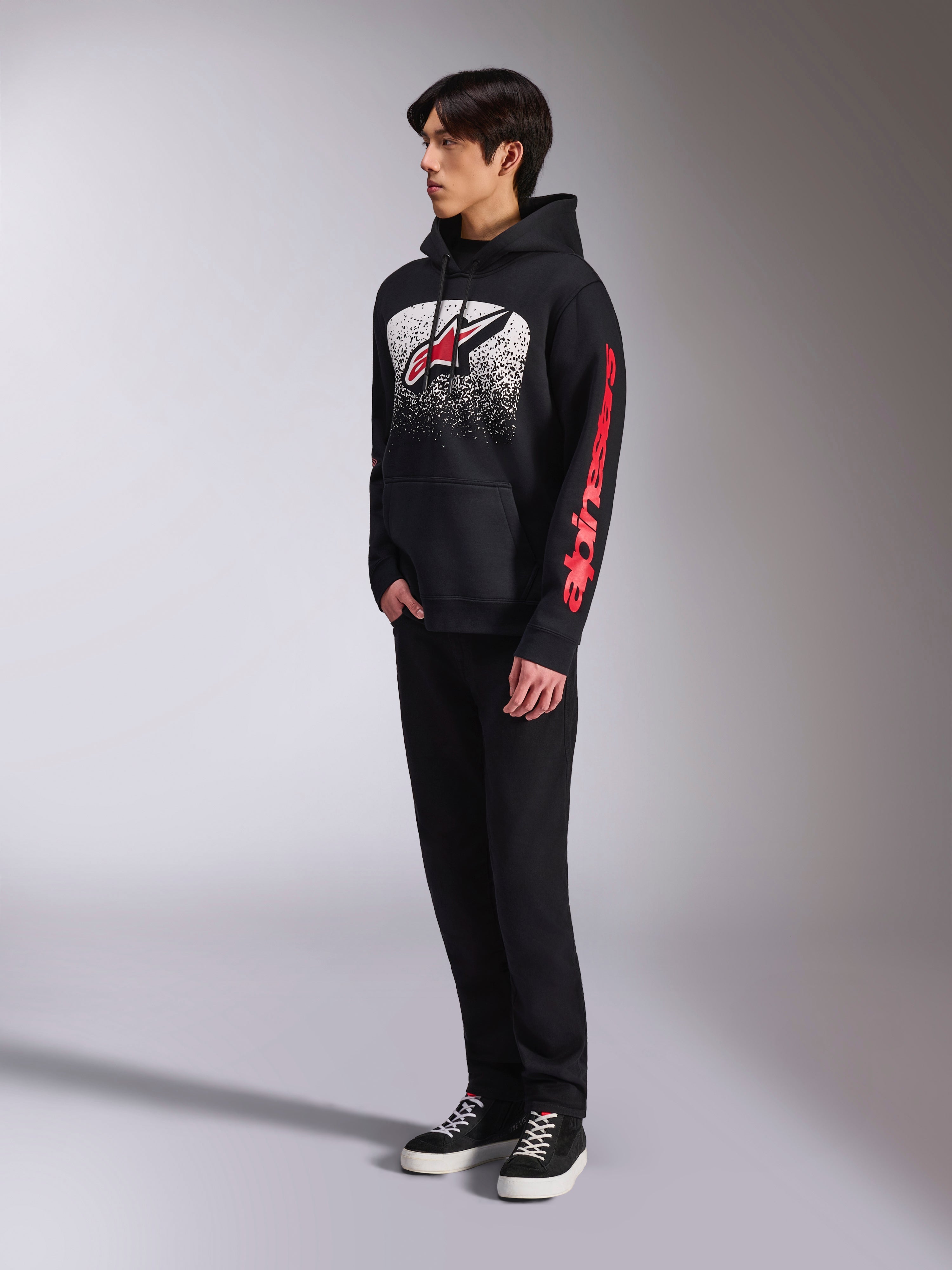 Alpinestars Obsessed hættetrøje, sort pullover-fleece, med en stor hvid plettet grafik på brystet, et rødt Astars-logo og rød branding på ærmerne, båret af en model med sorte bukser og sneakers, afslappet motorsport-streetwear