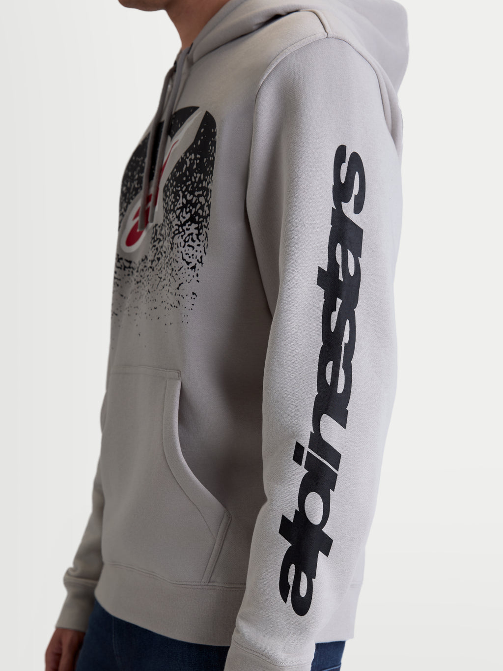 Alpinestars Obsessed hættetrøje, casual motorsportspullover i fleece, unisex, cementgrå og sort, sidevisning på model der fremhæver det lodrette Alpinestars-logo på ærmet og det MX-inspirerede gradientlogo på brystet, fremstillet i bomuld og genanvendt polyester.