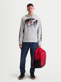 Alpinestars Obsessed Hættetrøje, herrehættetrøje i fleece til motorsport og fritid, cementgrå med rød og sort MX-inspireret gradientgrafik, branding på ærmerne, vist på mandlig model med rød rygsæk.