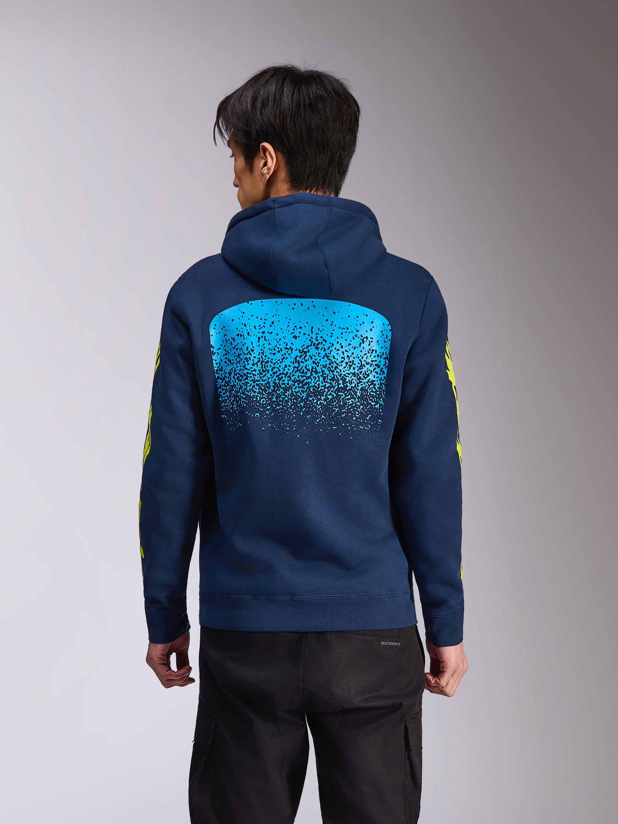 Alpinestars Obsessed Hoodie, marineblå hættetrøje i fleece, set bagfra med en stor lyseblå MX-gradueringsgrafik, gule Alpinestars-ordmærker på ærmerne, afslappet motorsport-inspireret streetwear