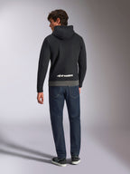 Alpinestars Parallel hættetrøje, mand set bagfra iført sort og gunmetal farveblokket pullover-fleece, hvidt Alpinestars ordlogo på den nederste del af ryggen, mørkeblå jeans, afslappet motorsport-inspireret streetwear