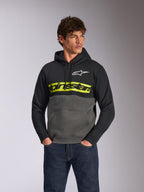 Alpinestars Parallel hættetrøje, afslappet farveblokket fleece-pullover, sort og gunmetal med en markant gul bryststribe, Alpinestars-tekstlogo og hvidt stjernelogo, båret af en mandlig model med mørkeblå jeans